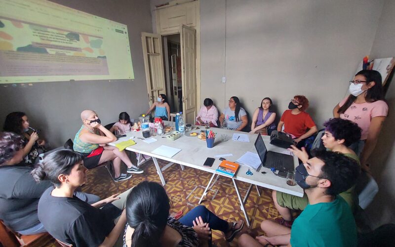 Capacitación con gente alrededor de una mesa viendo una presentación en powerpoint