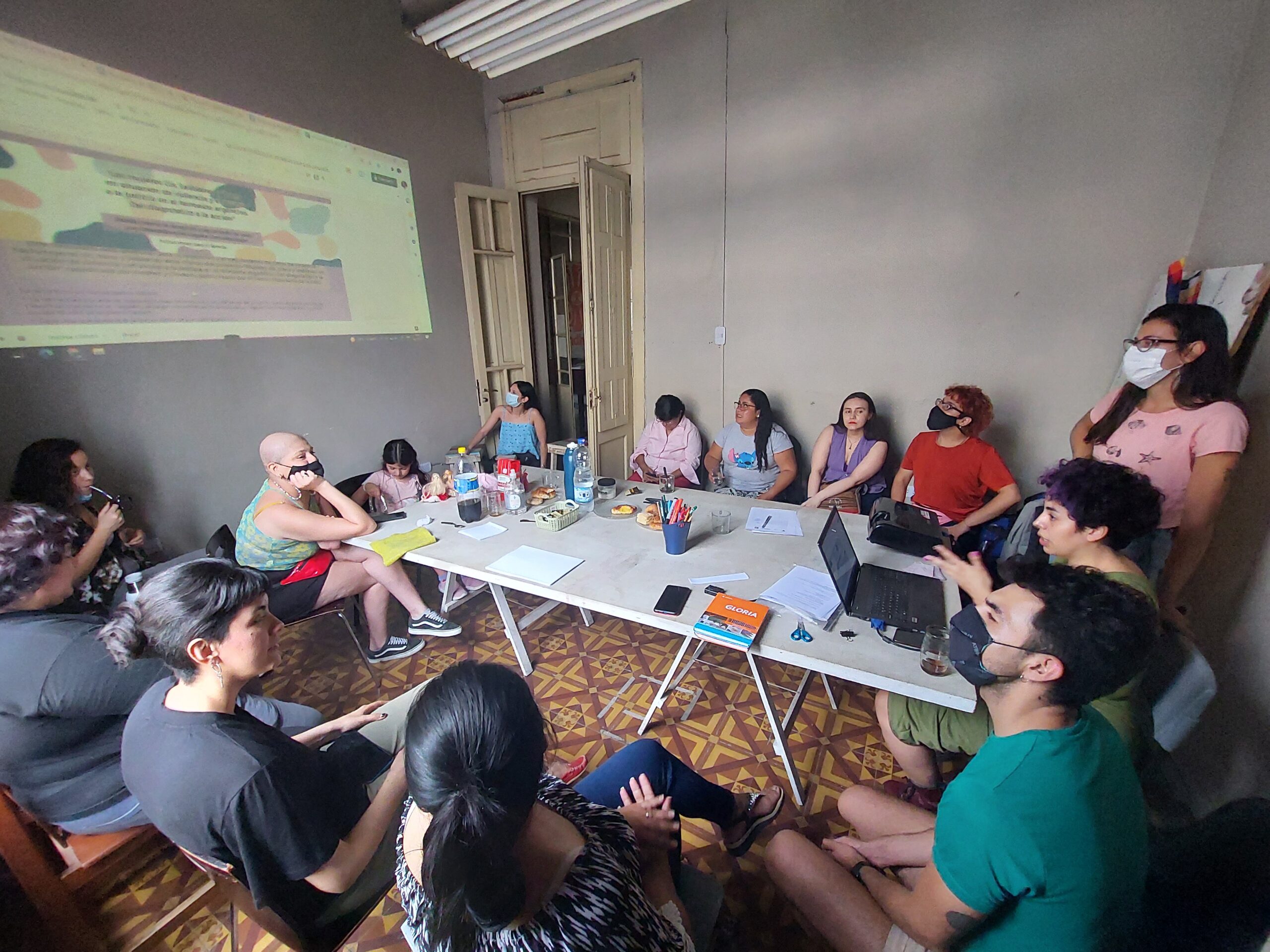 Capacitación con gente alrededor de una mesa viendo una presentación en powerpoint