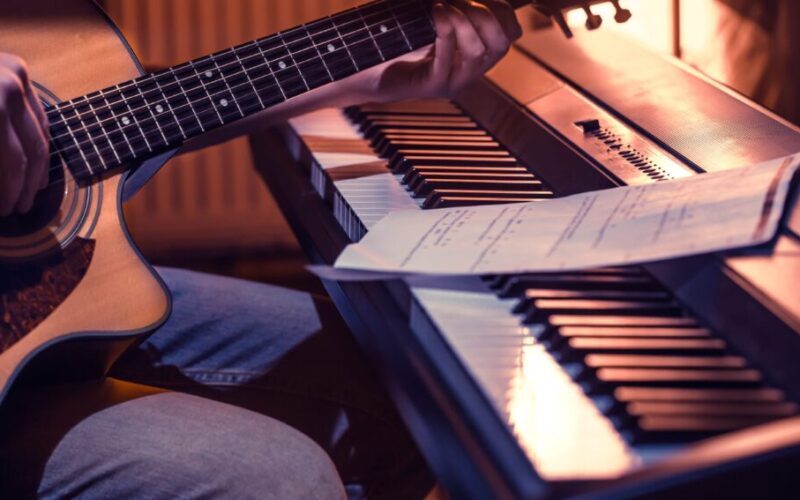 man playing acoustic guitar and piano close up recording notes beautiful color background music activity concept min 1024x567 1